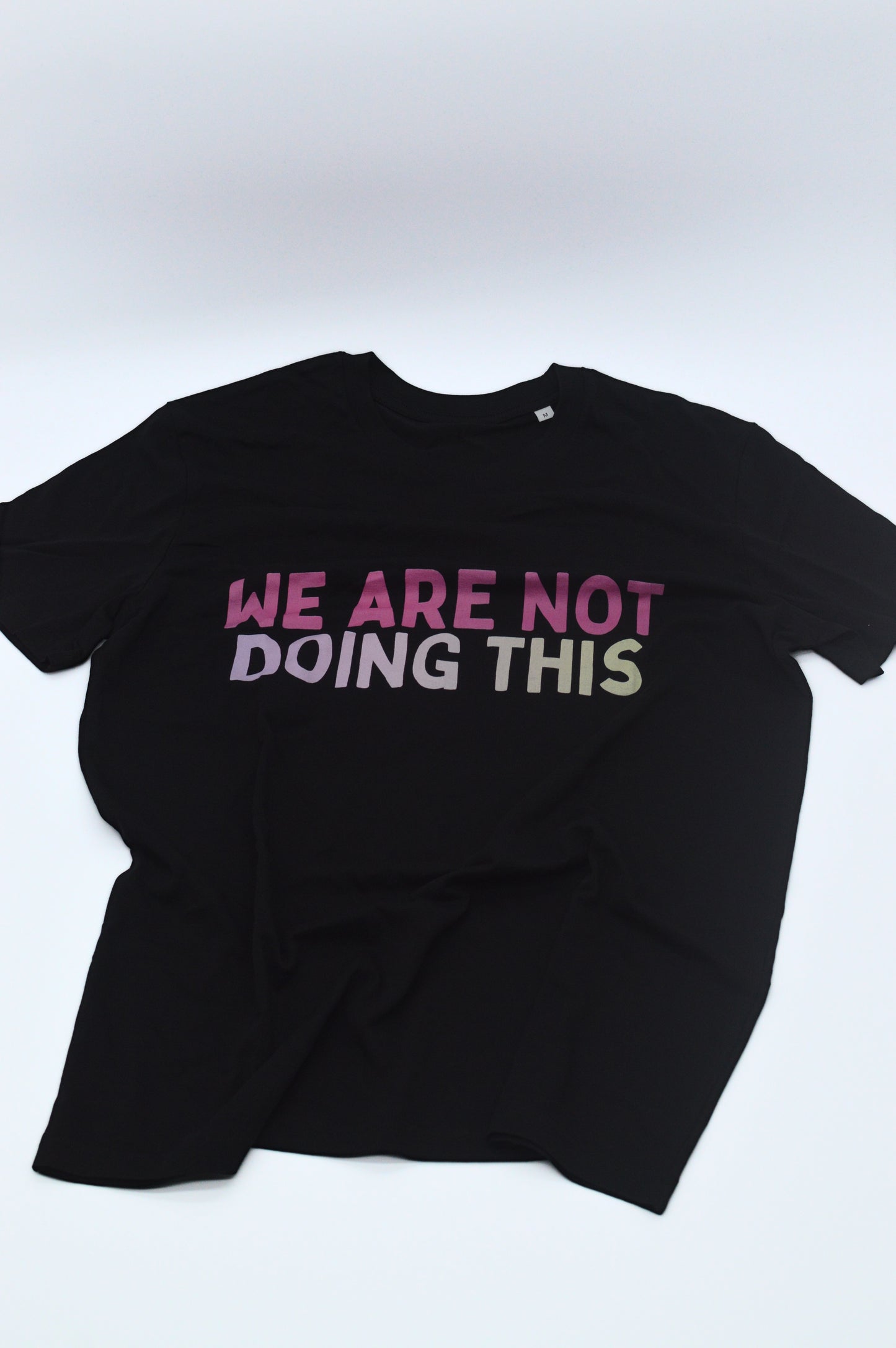 Black t-shirt with 'WE ARE NOT DOING THIS' slogan in colorful text, front view
