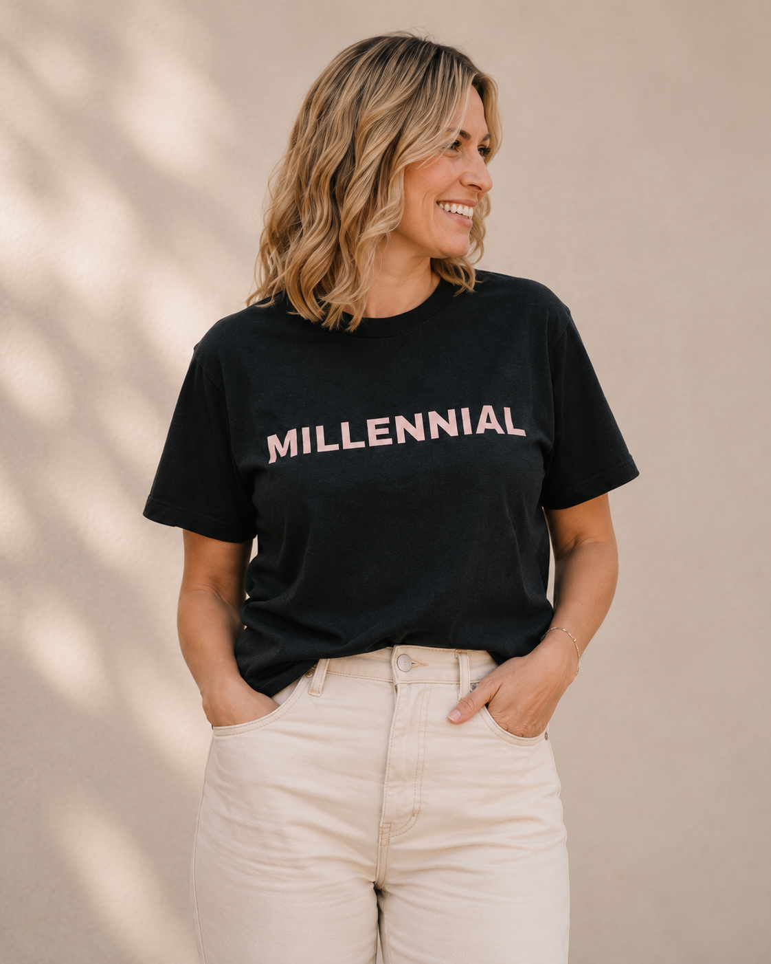 Close-up of woman wearing black 'MILLENNIAL' slogan t-shirt against a tan wall