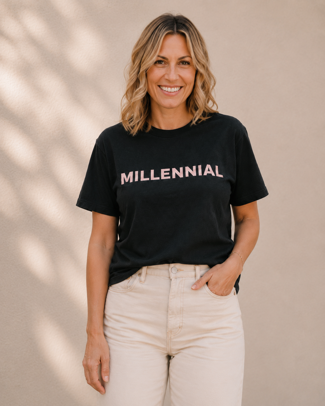 Woman wearing black t-shirt with 'MILLENNIAL' slogan in pink text, standing against a tan wall