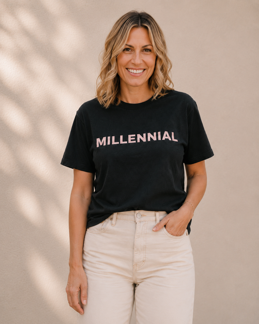 Woman wearing black t-shirt with 'MILLENNIAL' slogan in pink text, standing against a tan wall