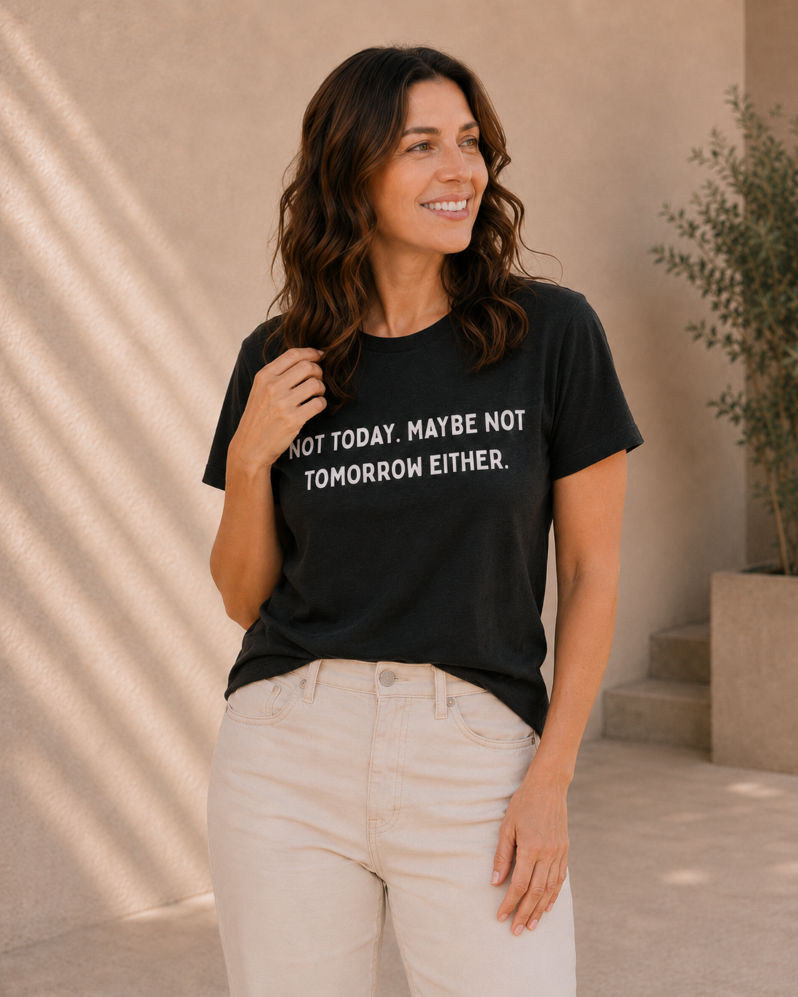 Close-up of woman wearing black 'NOT TODAY. MAYBE NOT TOMORROW EITHER' slogan t-shirt against a tan wall