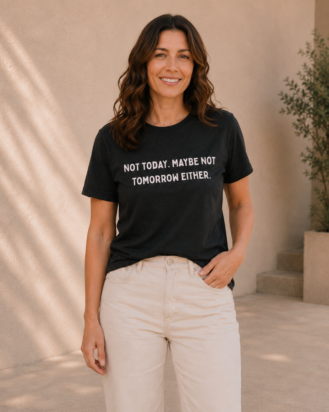 Woman wearing black t-shirt with white 'NOT TODAY. MAYBE NOT TOMORROW EITHER' slogan text, standing against a tan wall