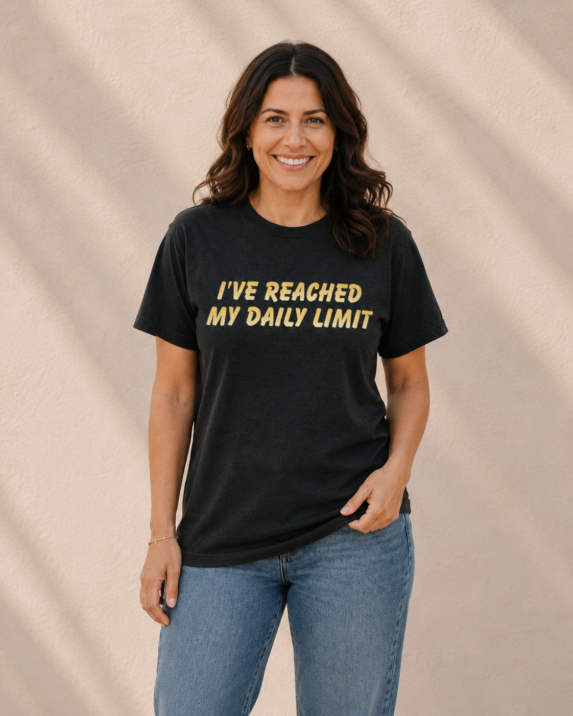 Woman wearing black t-shirt with yellow 'I'VE REACHED MY DAILY LIMIT' slogan text, standing against a tan wall