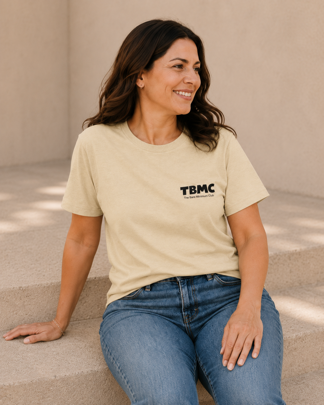 Woman wearing butter yellow TBMC logo t-shirt, alternate pose against a tan wall