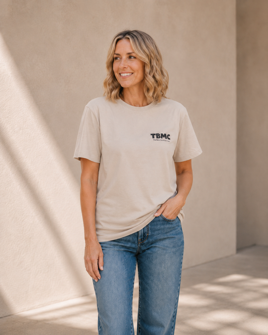 Woman wearing vintage white TBMC logo t-shirt, alternate pose against a tan wall