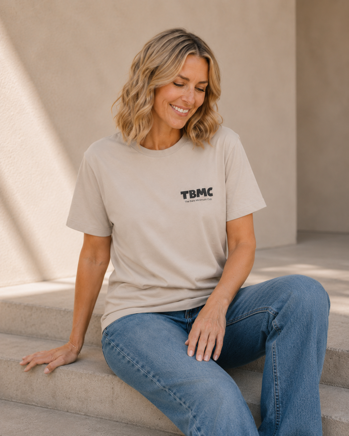 Close-up of woman wearing vintage white TBMC logo t-shirt against a tan wall