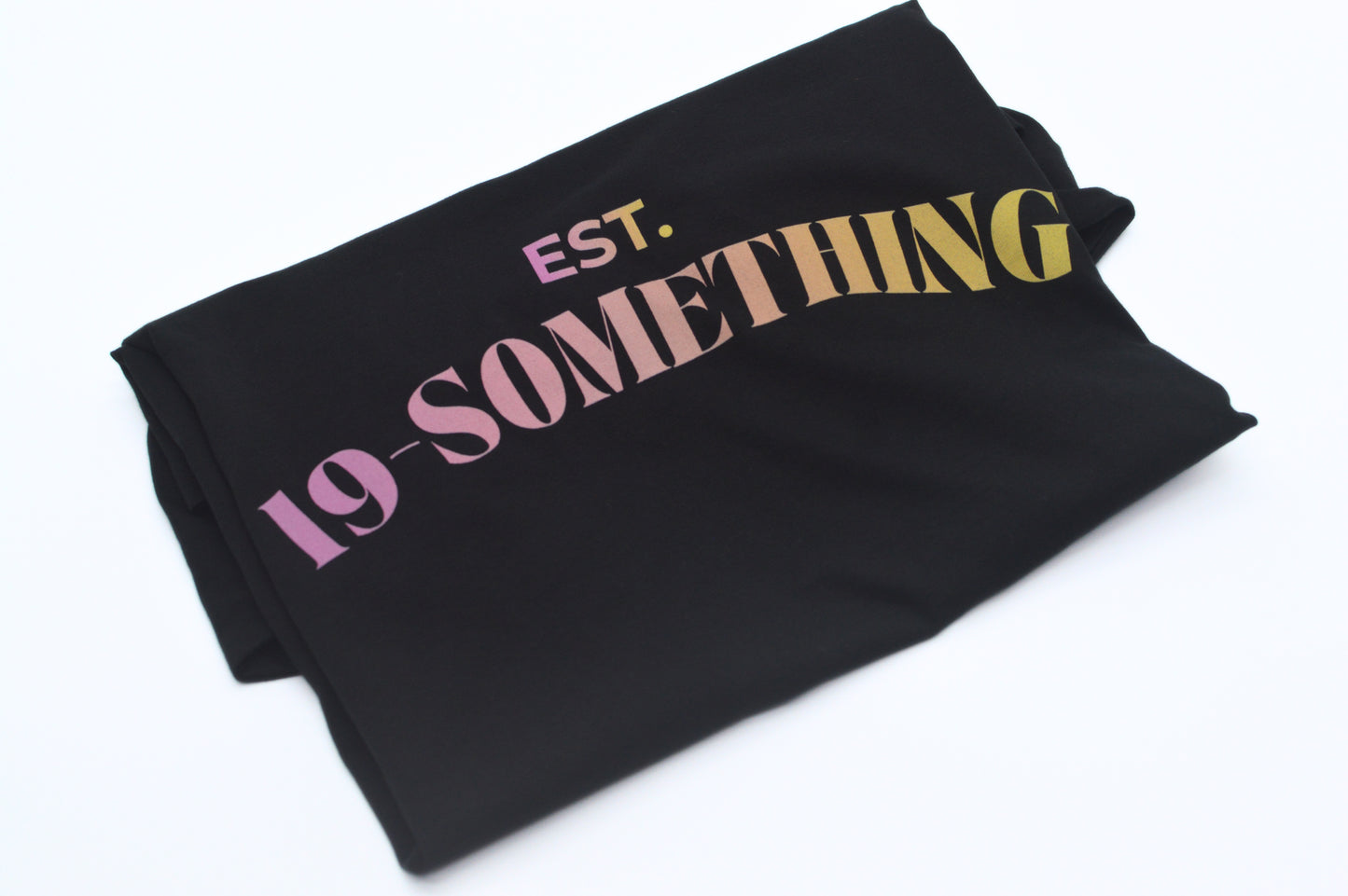 Folded Black t-shirt with 'EST. 19 SOMETHING' text on a white background