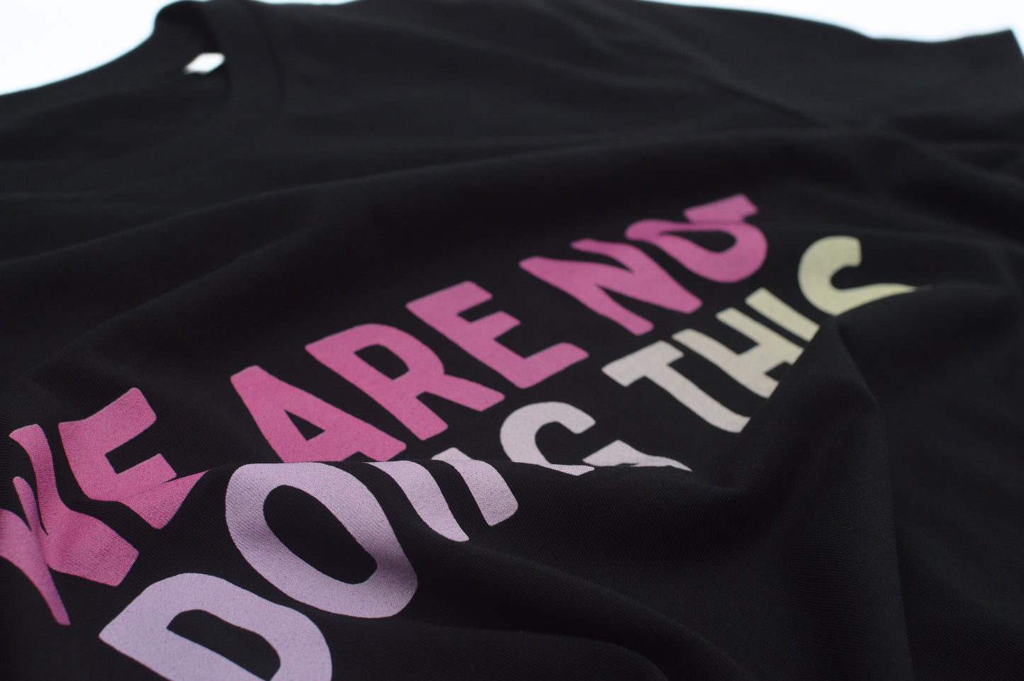 Closeup of Black t-shirt with colorful text 'WE ARE NOT DOING THIS' on a white background