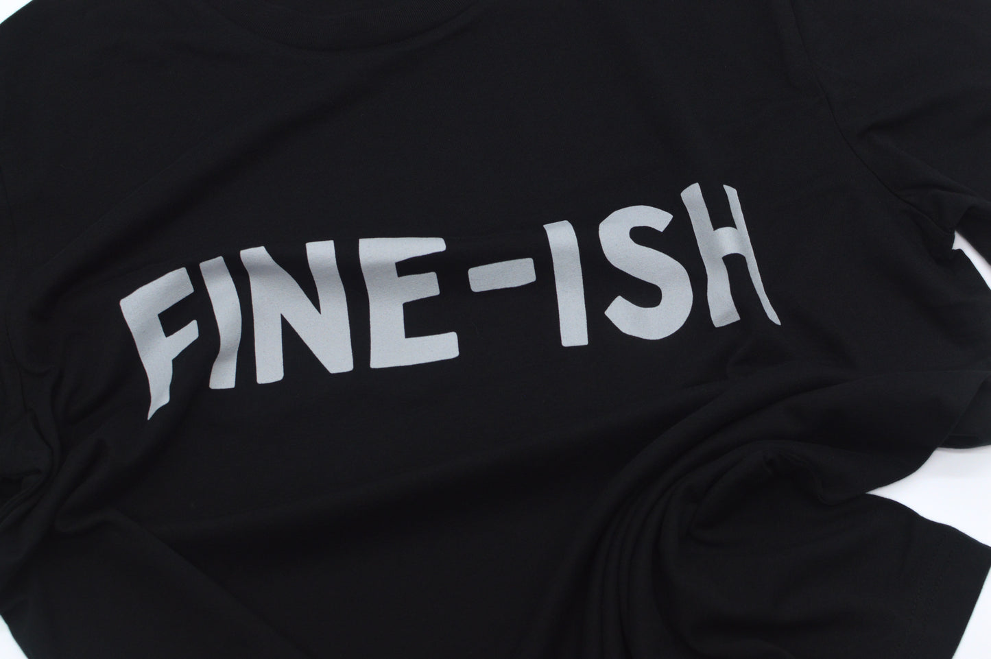 Closeup of Black  shirt with 'FINE-ISH' text on a white background