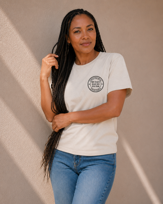 Woman wearing The Bare Minimum Club's vintage white 'My Face Has No Filter' graphic t-shirt, arms crossed, standing against a sunlit wall