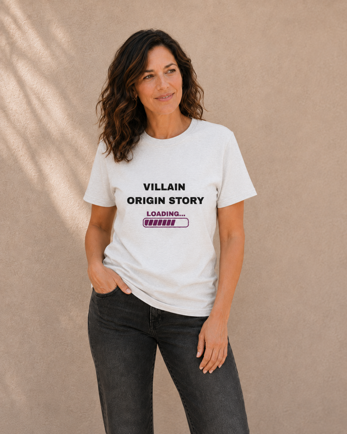 Woman modelling The Bare Minimum Club's white 'Villain Origin Story' t-shirt, smiling and touching her hair in natural light
